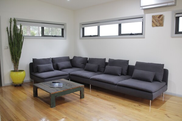 A modern living room with a grey sectional sofa, a wooden coffee table, and a large potted plant. - Dacelo (Halls Gap)