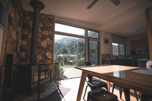 A modern kitchen with large windows, a stone fireplace, and a dining area with a wooden table and chairs. - Dacelo (Halls Gap)