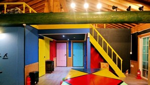 Une pièce aux couleurs vives, dotée d’un motif géométrique sur le sol, d’un escalier avec des rampes jaunes et d’un extincteur près de la porte.
