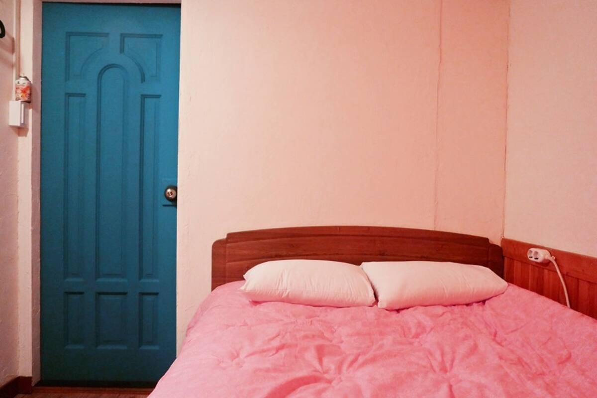 A bedroom with a wooden headboard, a pink bedspread, and a blue door.