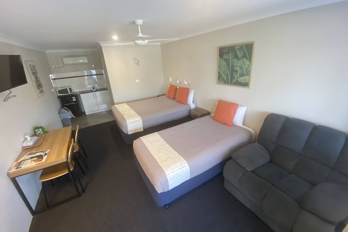 A hotel room with two single beds, a sofa, a desk with chairs, and a kitchenette.