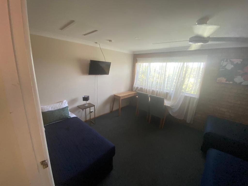 A room with a bed, a desk, a chair, and a television mounted on the wall.