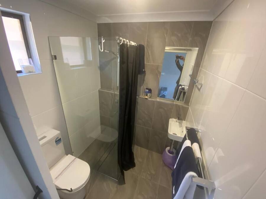 A bathroom with a glass-enclosed shower, a toilet, a sink with a mirror, and a towel rack.