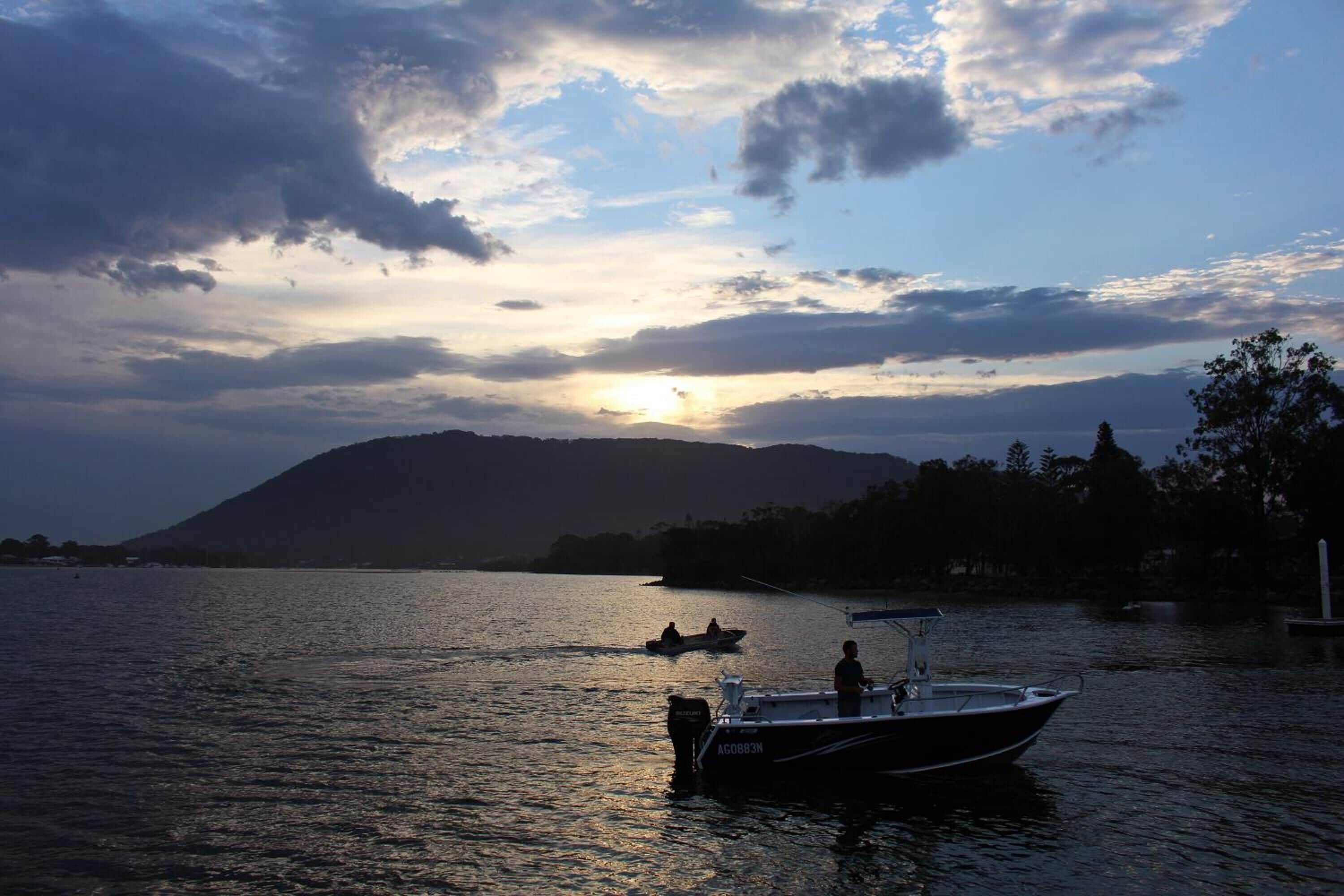 Un barco amarrado en un lago tranquilo con un atardecer de fondo y la silueta de una montaña.