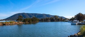 A calm lake with boats docked on the right, surrounded by trees and a mountain in the background. - Woongarra Motel (North Haven)