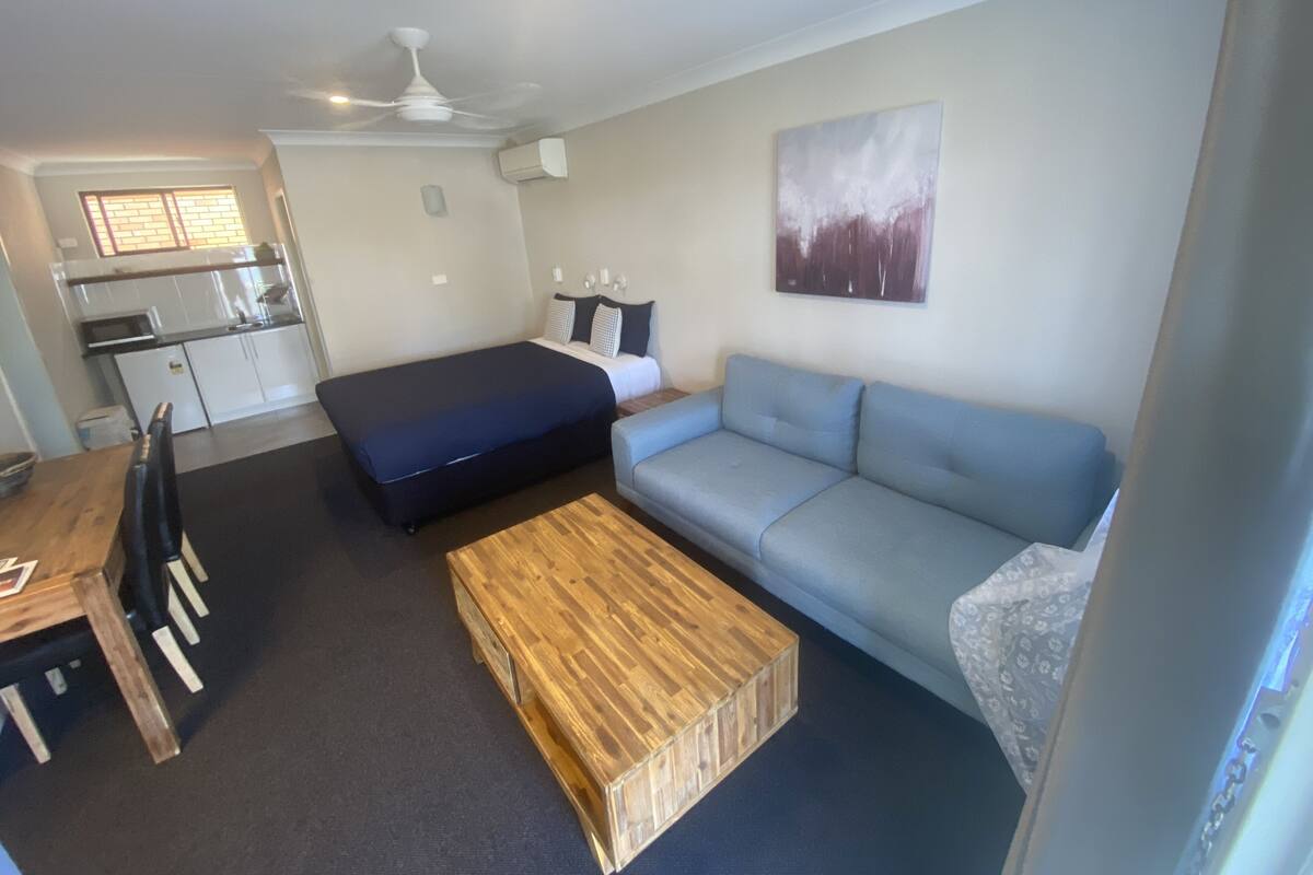 A compact living space with a bed, sofa, dining table, and kitchenette.