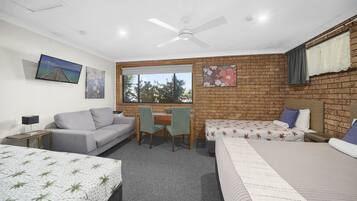A room with a brick wall, a desk, two beds, a sofa, and a ceiling fan.