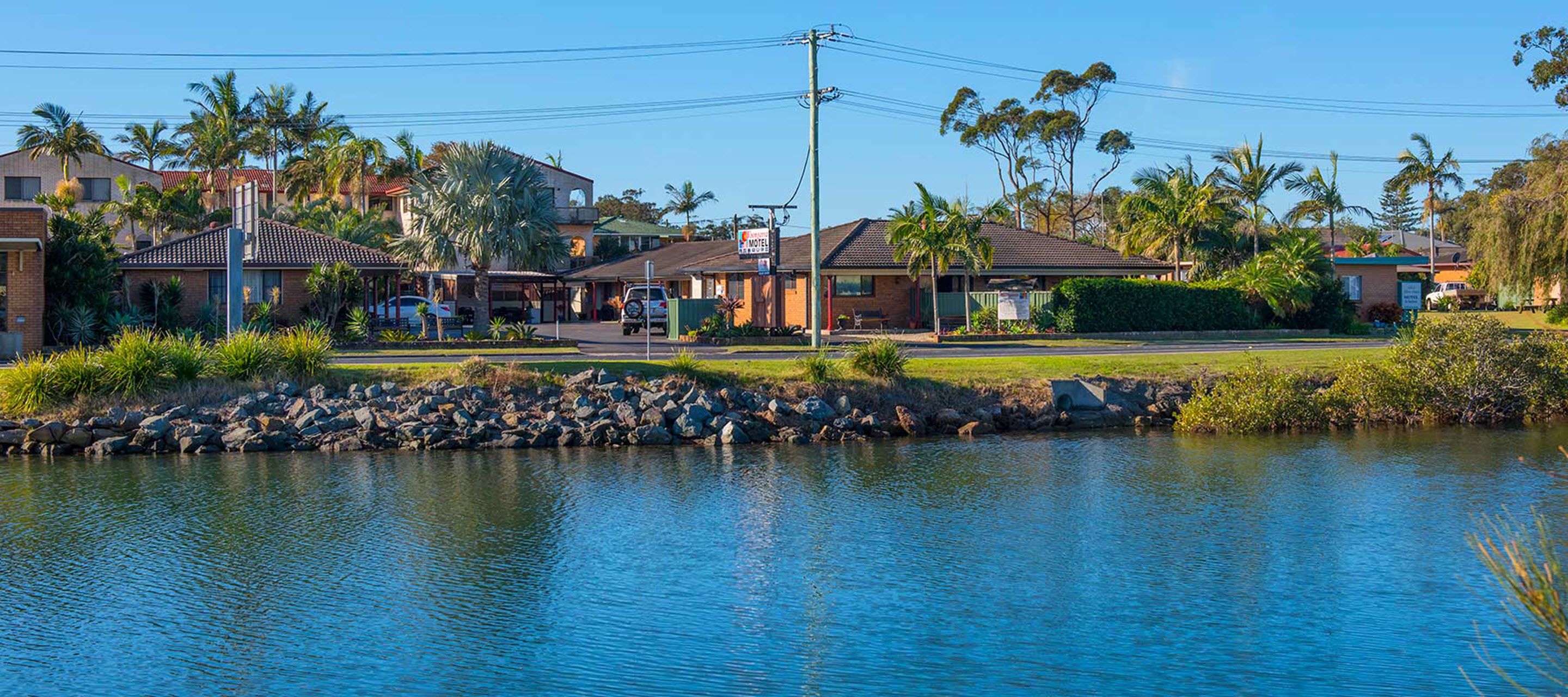 A motel with a swimming pool, surrounded by palm trees and a clear blue sky.