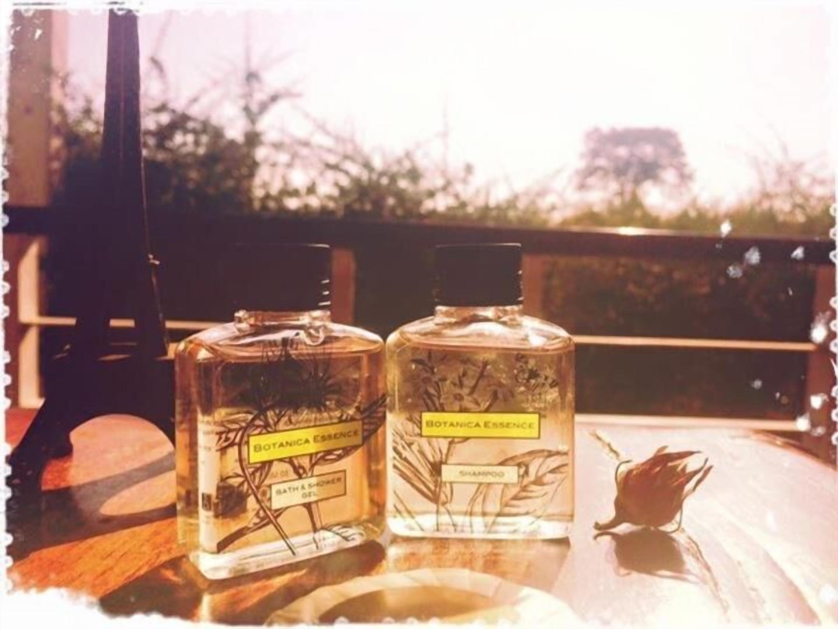 Dos botellas de gel de baño y ducha y champú Botanica Essence sobre una mesa de madera con una barandilla al fondo.