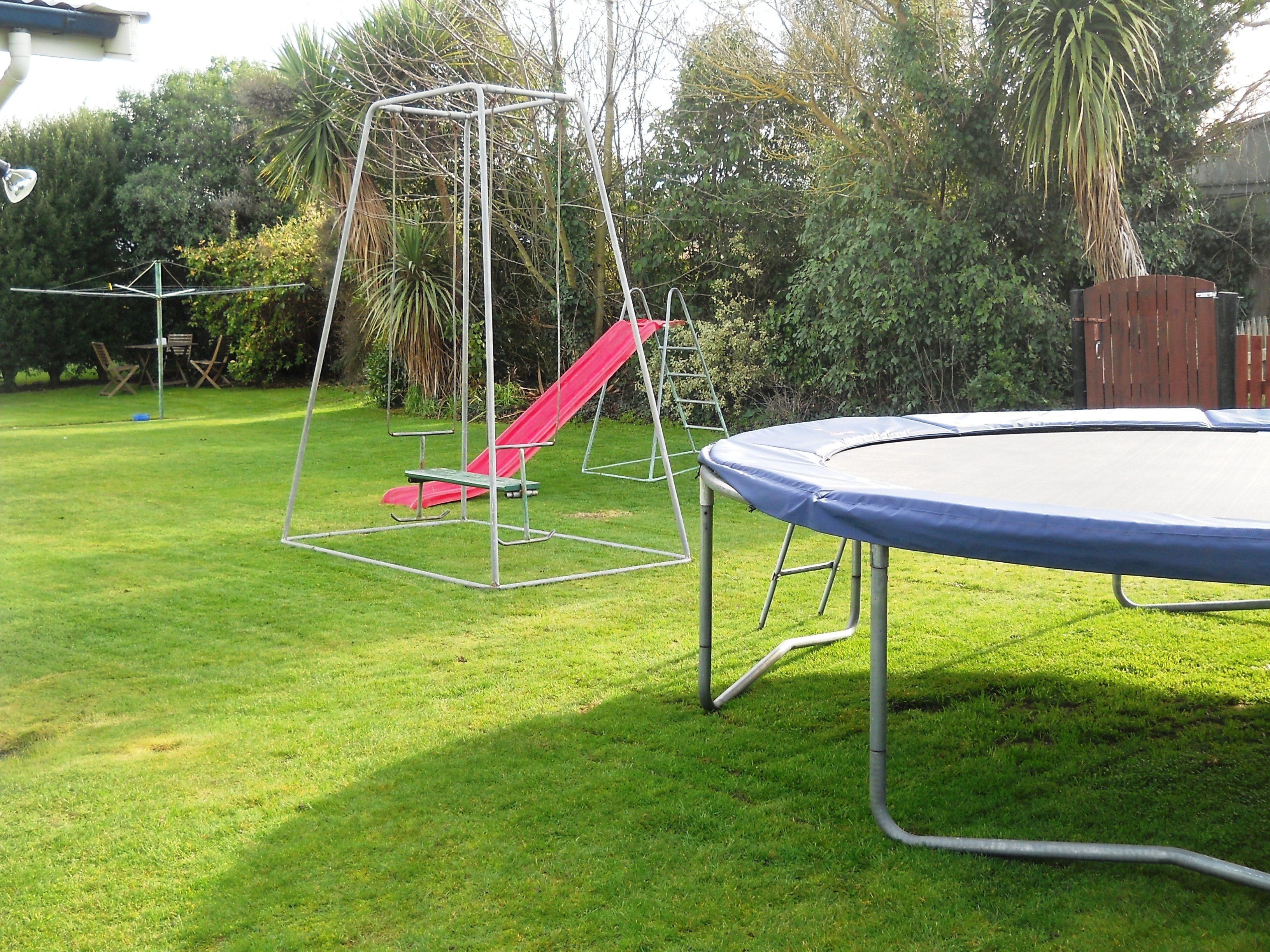 A backyard with a trampoline, a swing set, and a red slide.