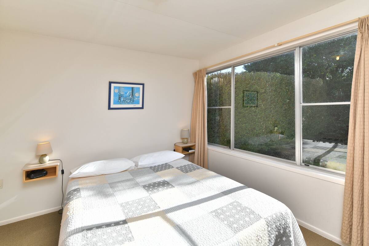 Quarto com uma cama grande, duas mesas de cabeceira com luminárias, um quadro na parede e uma janela com cortinas.