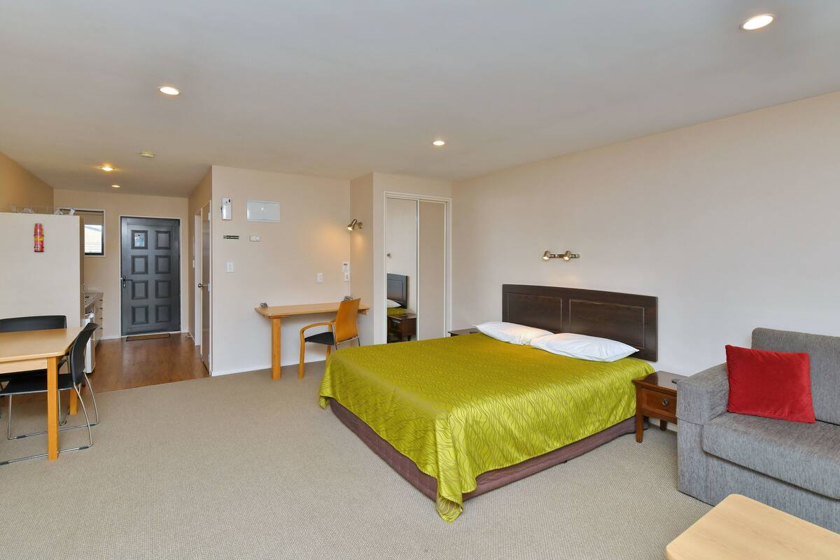 Quarto com cama, escrivaninha, cadeira, sofá e mesinha.