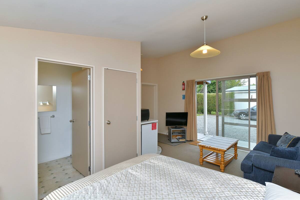 Quarto de hotel com cama, sofá, televisão, mesinha e janela com vista para o exterior.