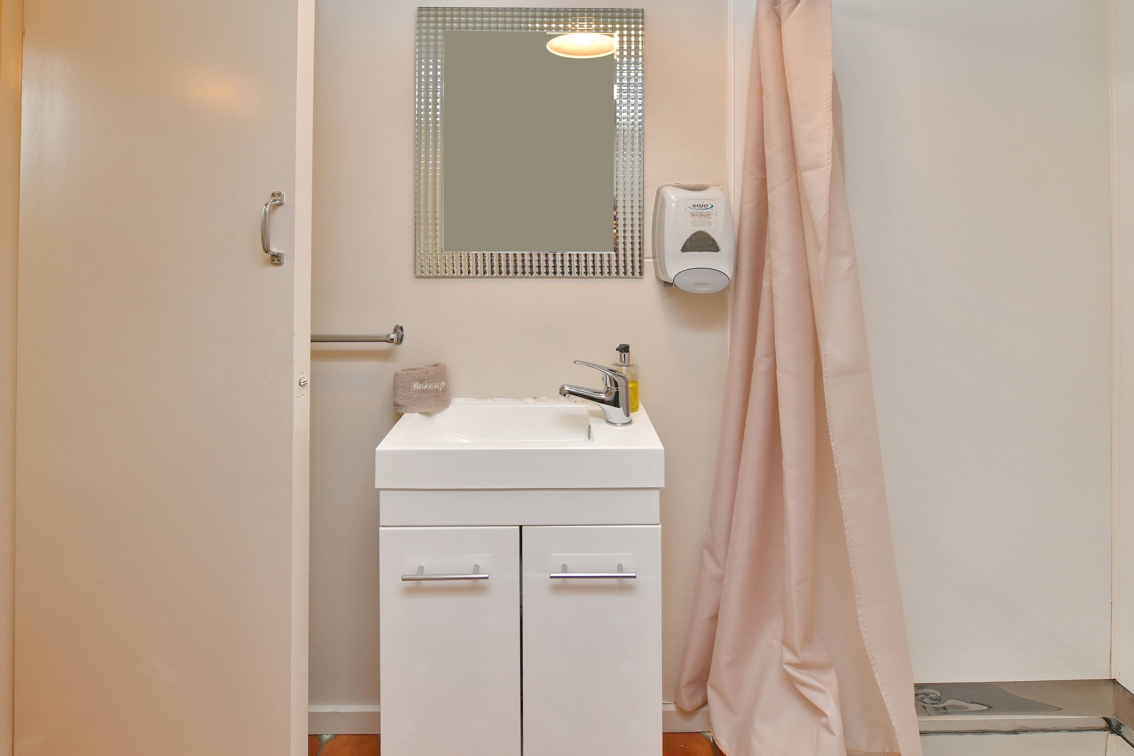 A bathroom with a white sink, a mirror, a soap dispenser, and a shower curtain.