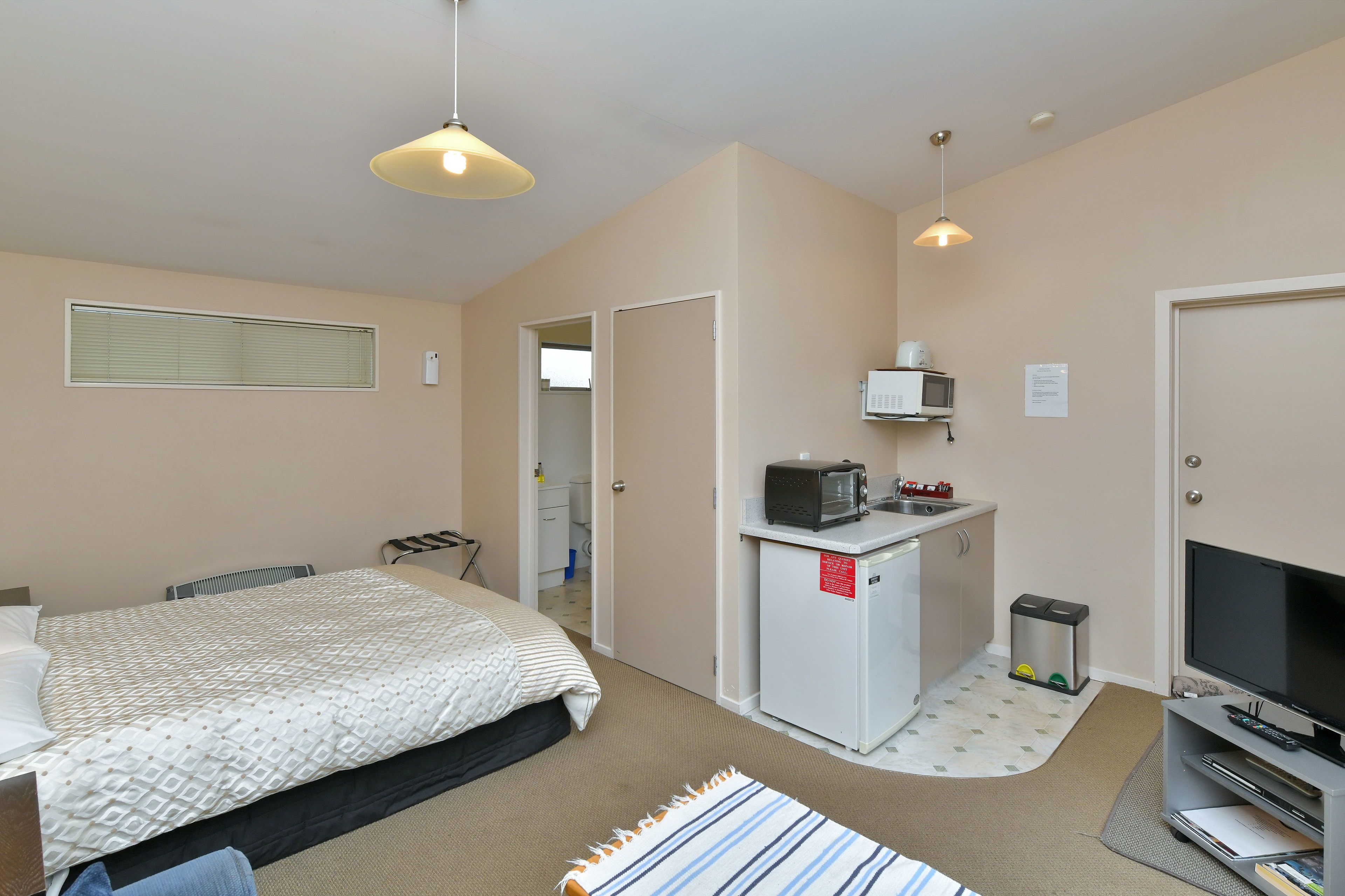 A compact hotel room with a bed, a small kitchenette, a TV, and a microwave.