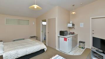 A compact hotel room with a bed, a small kitchenette, a TV, and a microwave.