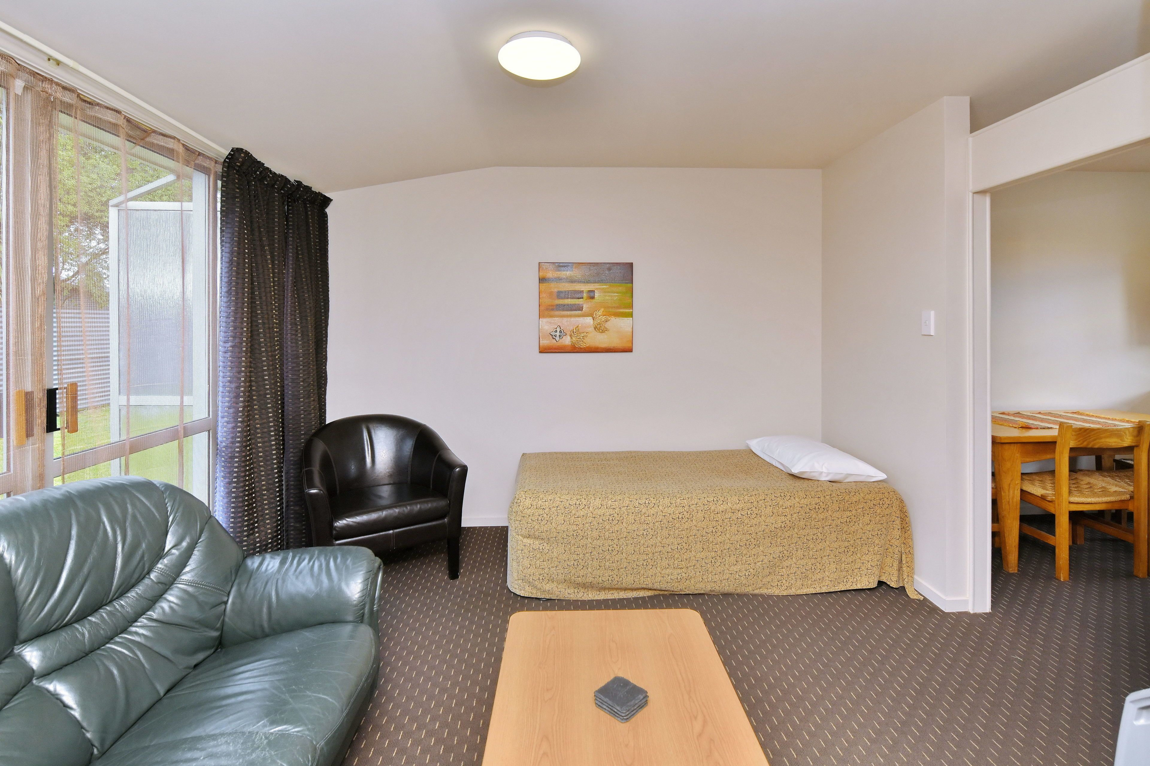 Habitación pequeña con una cama individual, un sofá, una silla, una mesita y un cuadro en la pared.