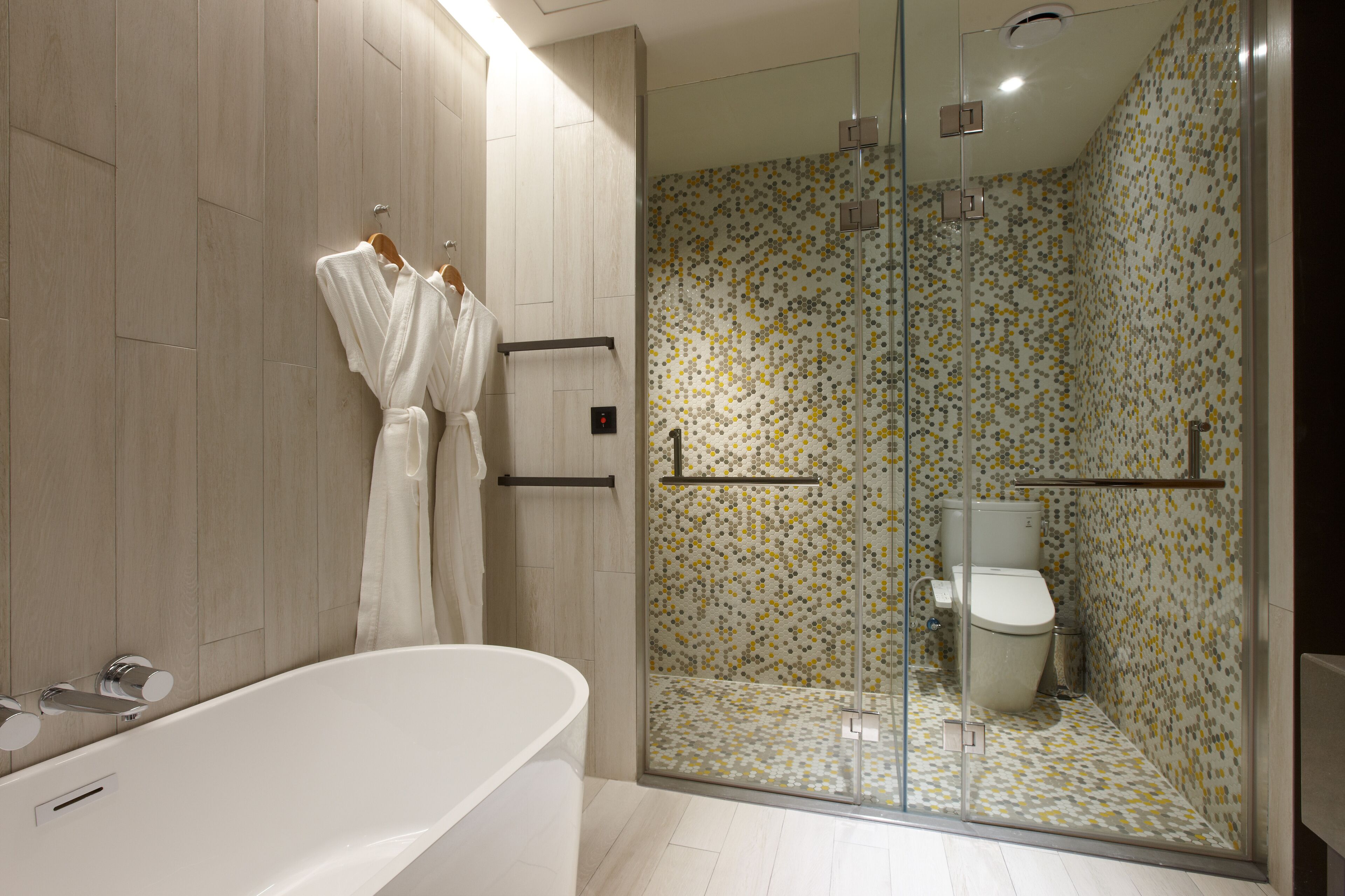 Un baño moderno con una bañera independiente, una ducha con cerramiento de vidrio y un inodoro con un revestimiento de azulejos estampados.
