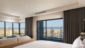 Ein modernes Hotelzimmer mit einem großen Bett, einer Couch und Blick auf die Stadt durch große Fenster.