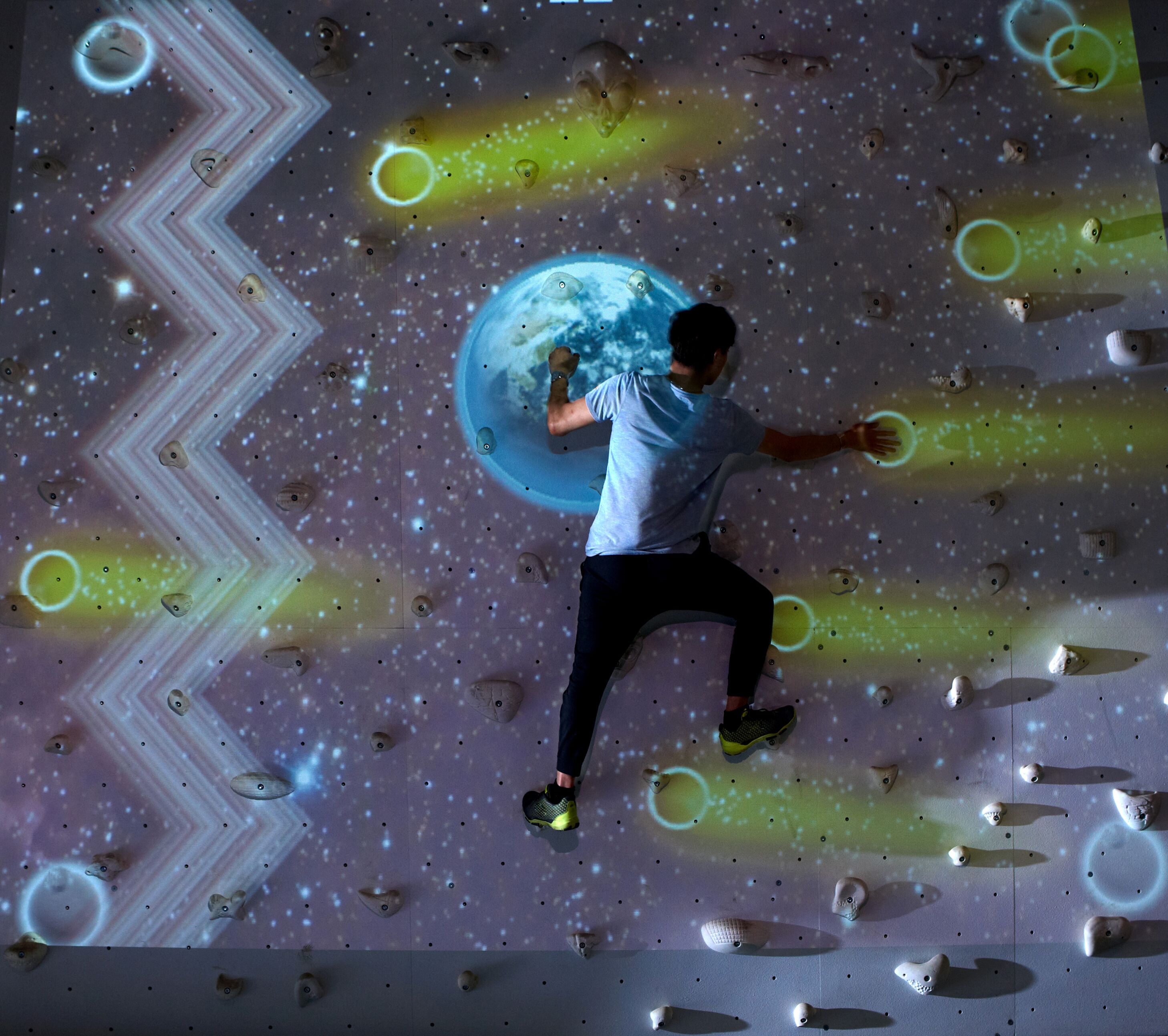 Una persona escala una pared con un diseño único y futurista que presenta patrones geométricos y círculos brillantes.