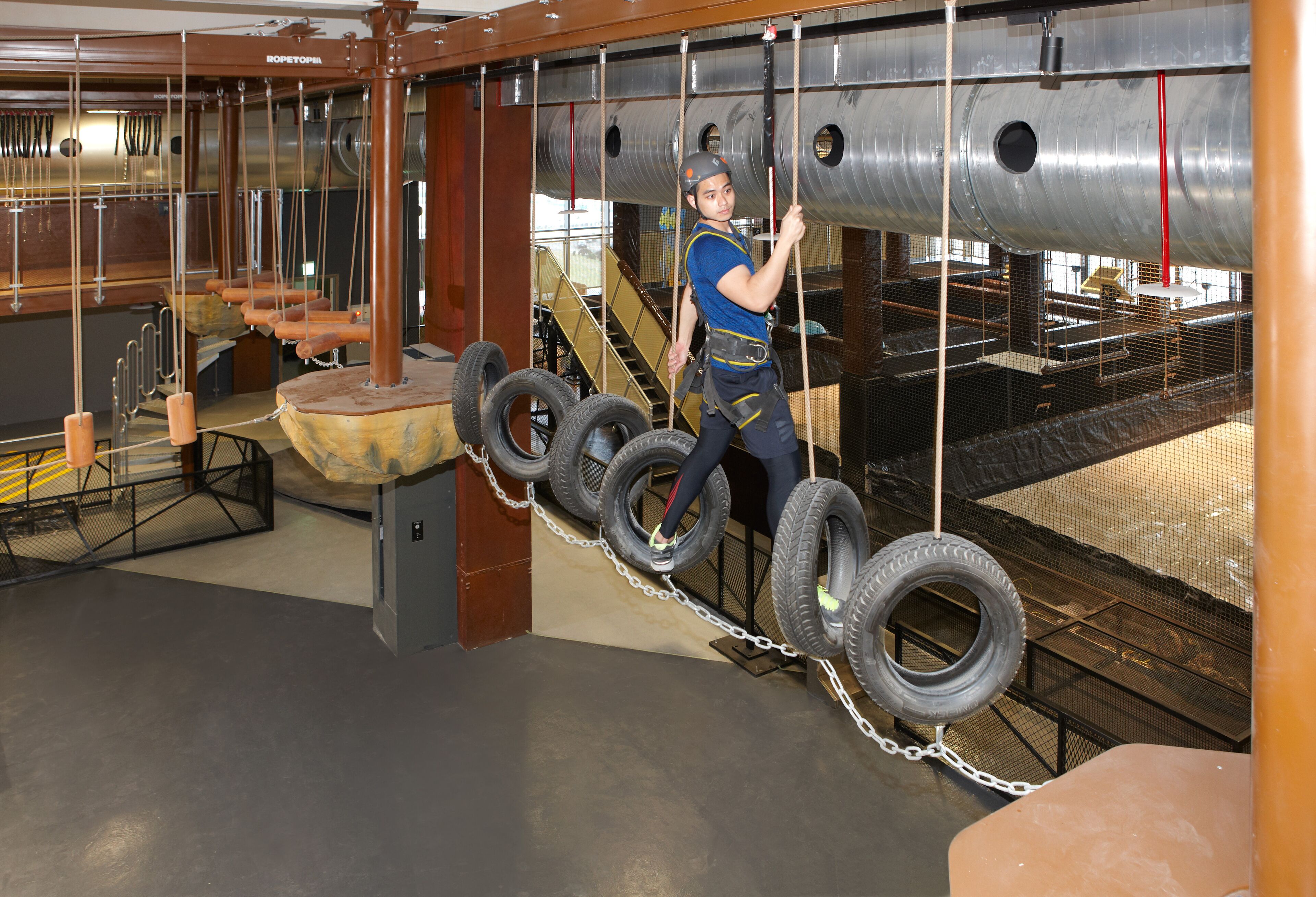 A person navigating a rope course with tire obstacles.