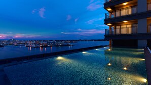 Ein modernes Hotel mit einem Dachpool im Infinity-Stil, der auf einen Hafen in der Abenddämmerung blickt.