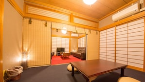 Ein traditioneller japanischer Raum mit Tatami-Bodenbelag, einem niedrigen Holztisch, einer Couch und Schiebetüren mit Shoji-Bildschirmen.