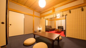 Ein traditioneller japanischer Raum mit Tatami-Bodenbelag, einem niedrigen Tisch, Kissen und Schiebetüren.