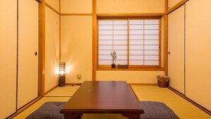 Ein traditioneller japanischer Raum mit Tatami-Boden, einem niedrigen Tisch, Schiebetüren und einem Fenster mit Shoji-Bildschirmen.
