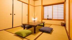 Ein traditioneller japanischer Raum mit Tatami-Böden, einem niedrigen Tisch, Kissen und verschiebbaren Türen.