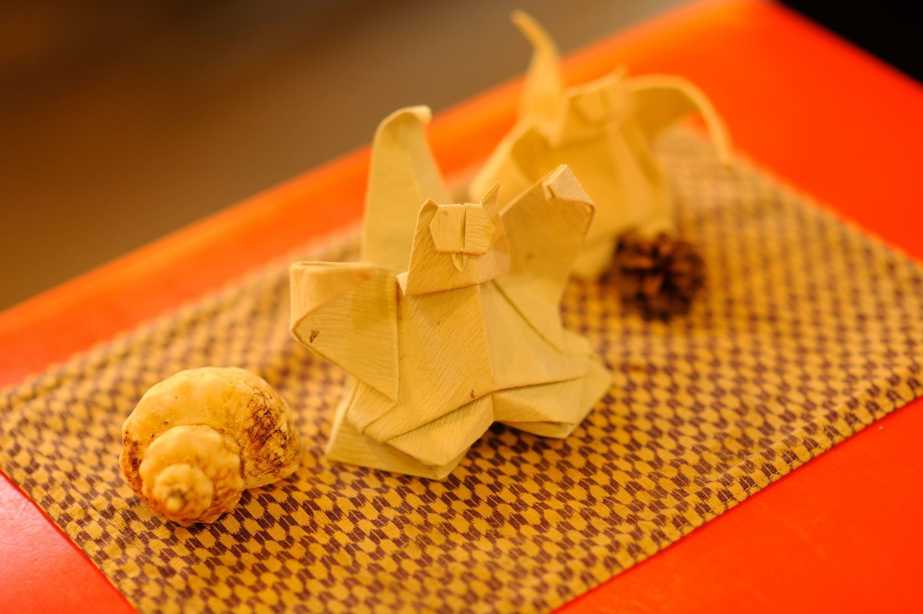 Un arreglo decorativo con un tapete tejido, una pequeña piña y dos figuras de origami.