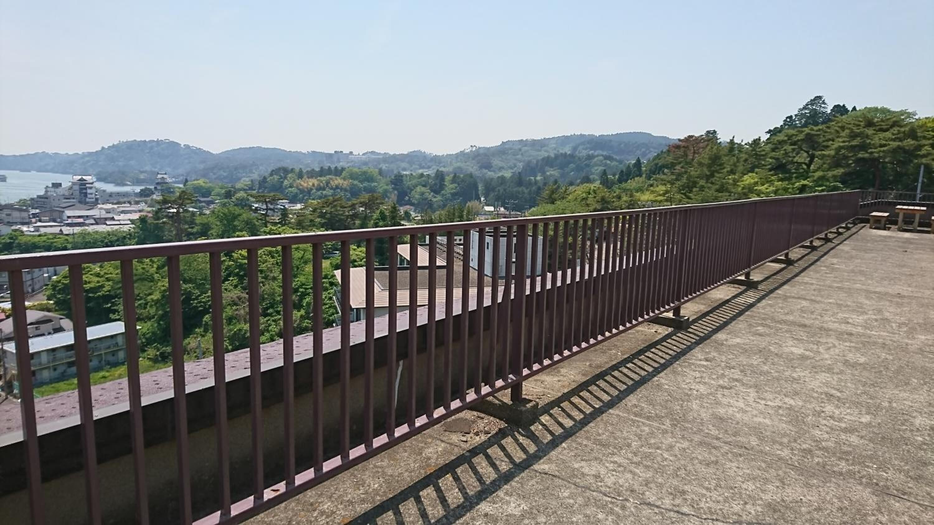 A concrete balcony with a metal railing overlooking a cityscape with buildings and hills.