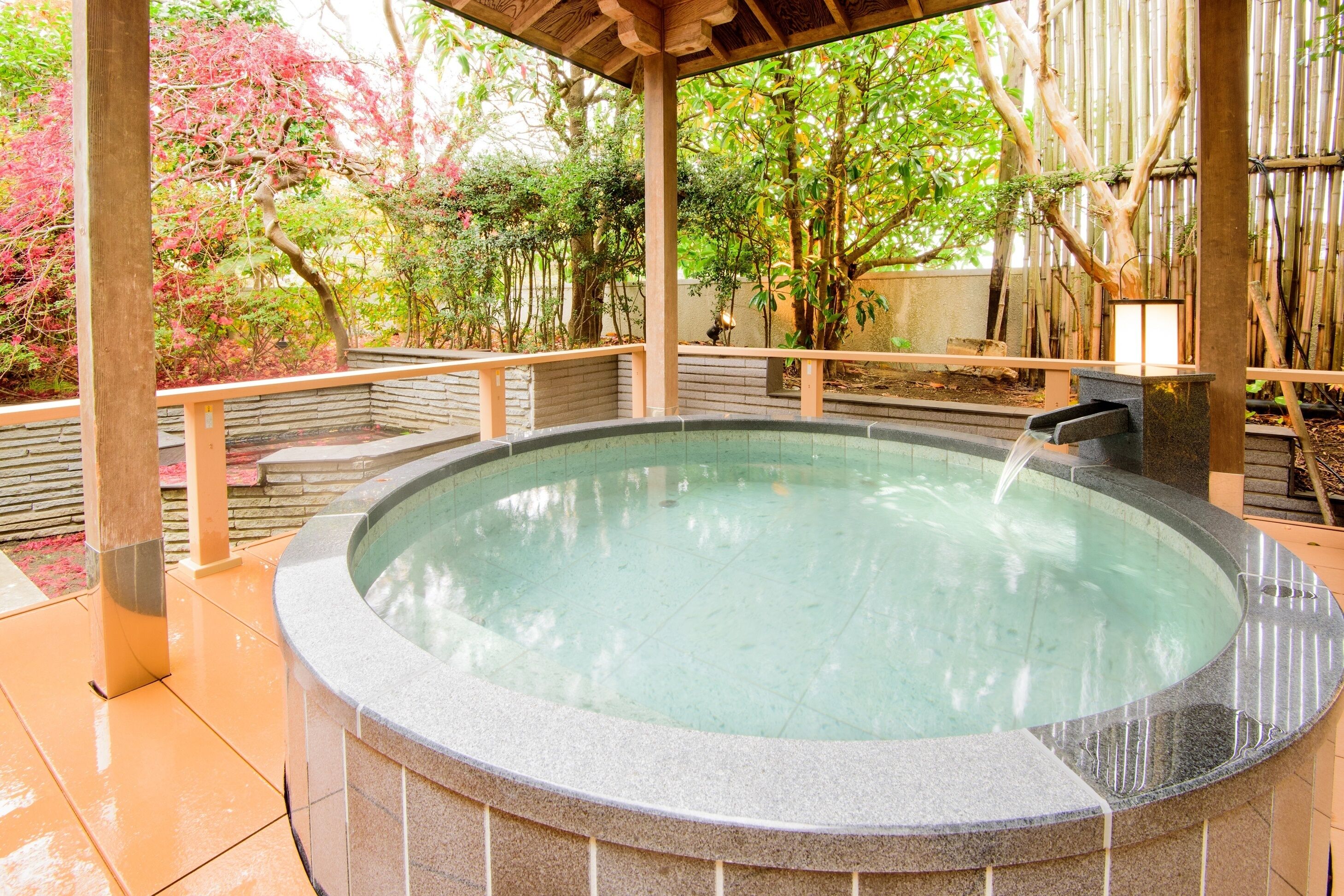 Un jacuzzi con una pérgola de madera y baldosas de piedra, rodeado de exuberante follaje y bambú.