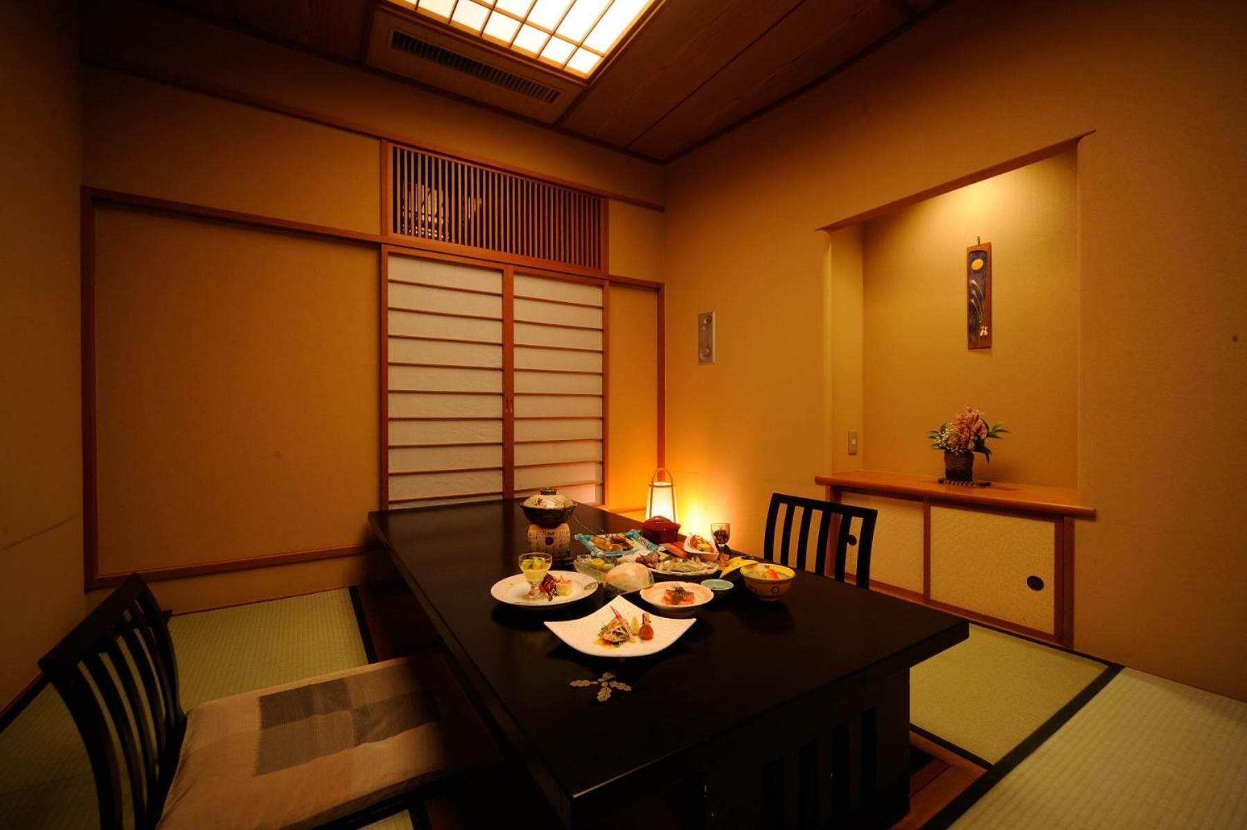 Une salle à manger de style japonais traditionnel, avec des tatamis servant de sièges, une table basse dressée avec divers plats, et une lumière douce créant une ambiance chaleureuse.