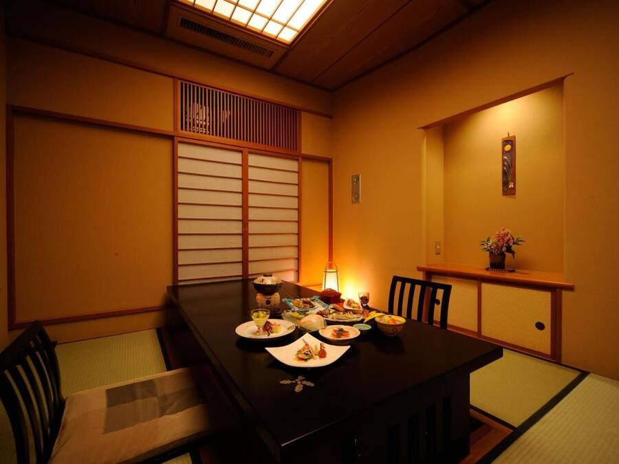 Une salle à manger de style japonais traditionnel, avec des tatamis servant de sièges, une table basse dressée avec divers plats, et une lumière douce créant une ambiance chaleureuse.