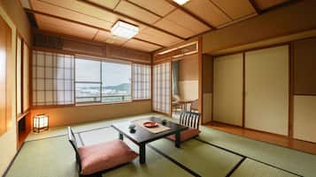 Ein traditioneller japanischer Raum mit Tatami-Böden, einem niedrigen Tisch mit Kissen, Schiebetüren und Blick auf eine Stadtlandschaft.