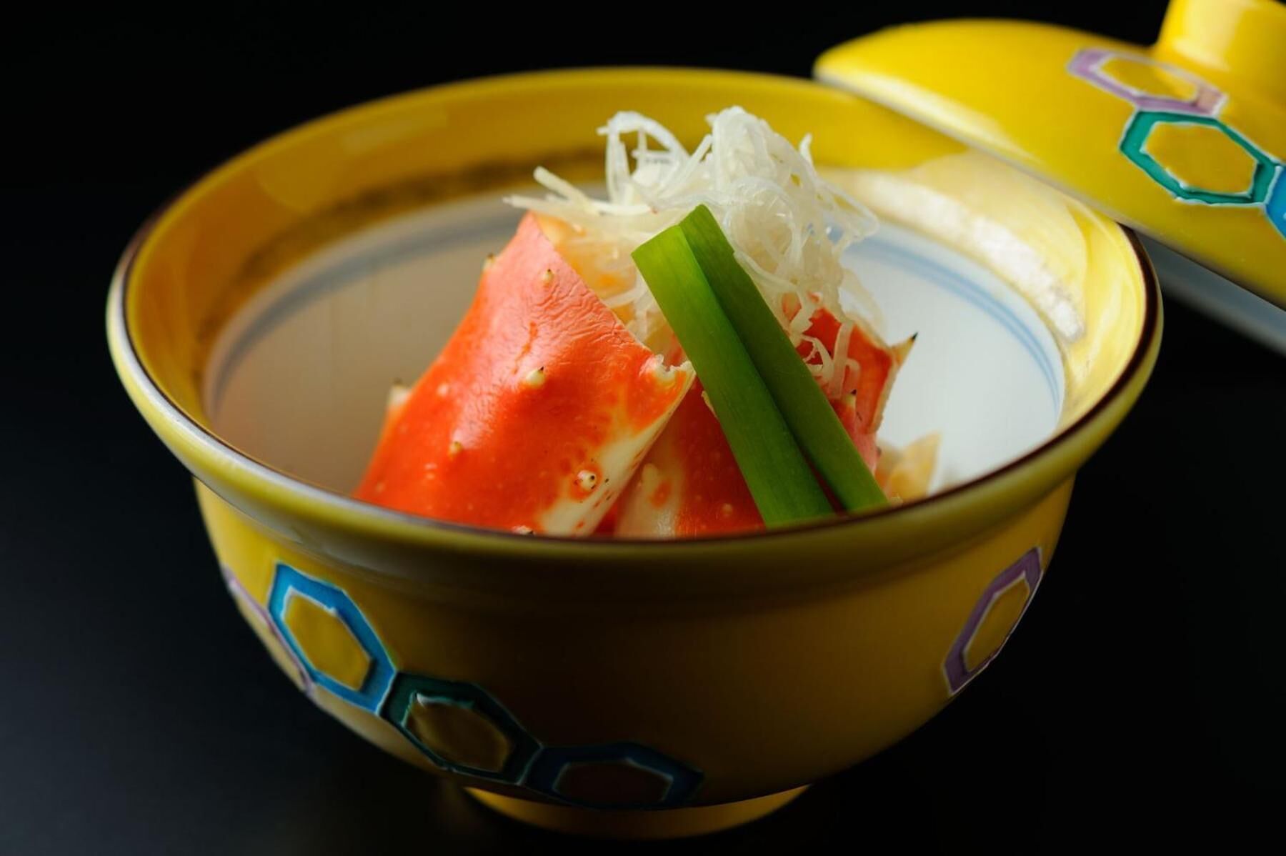 A bowl of soup with a piece of salmon and green onions.