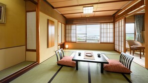 A traditional Japanese room with tatami flooring, a low table with cushions, and sliding doors leading to a balcony with a view. - Shintomi-tei (Matsushima)