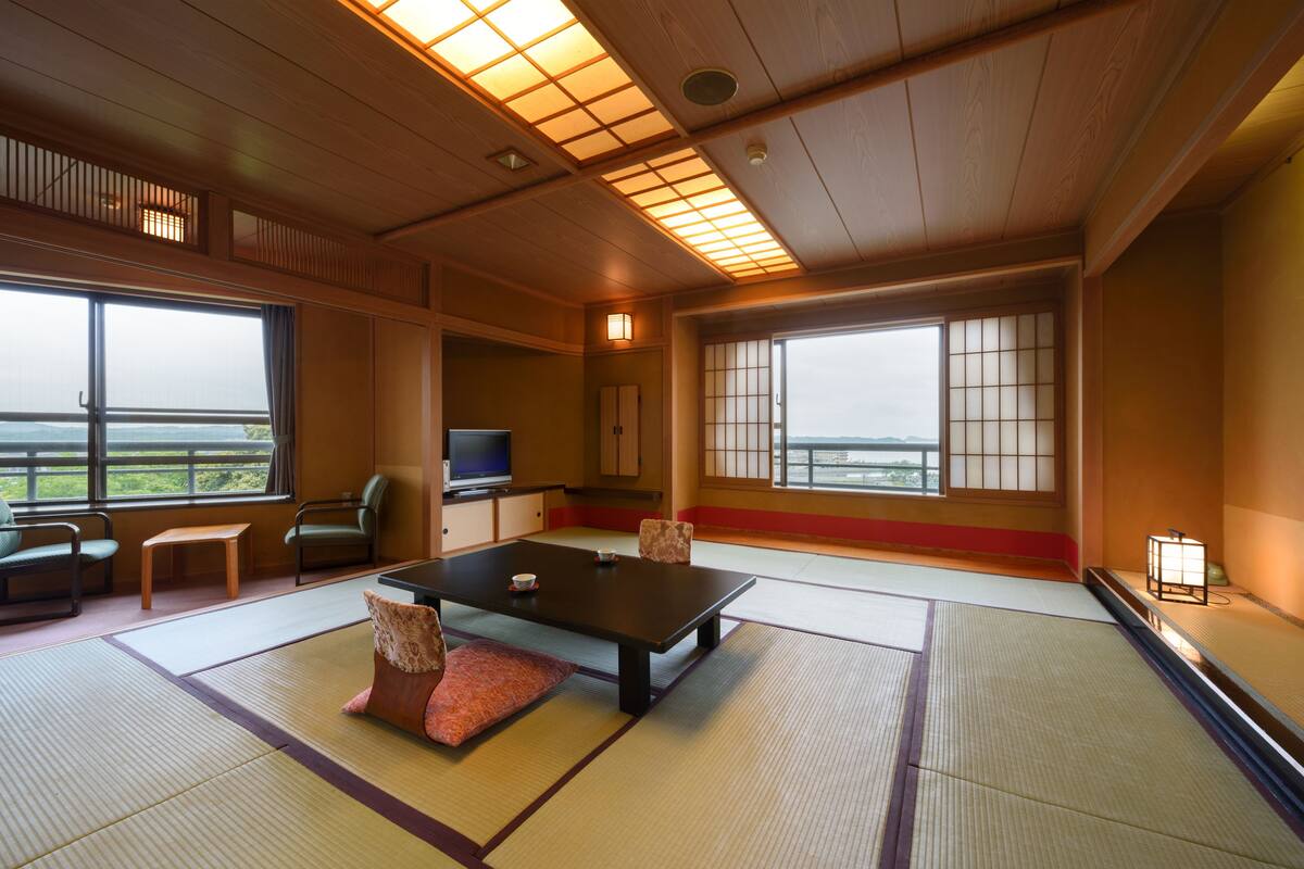 A tatami mat room with a low table, cushions, a television, and large windows offering a view.