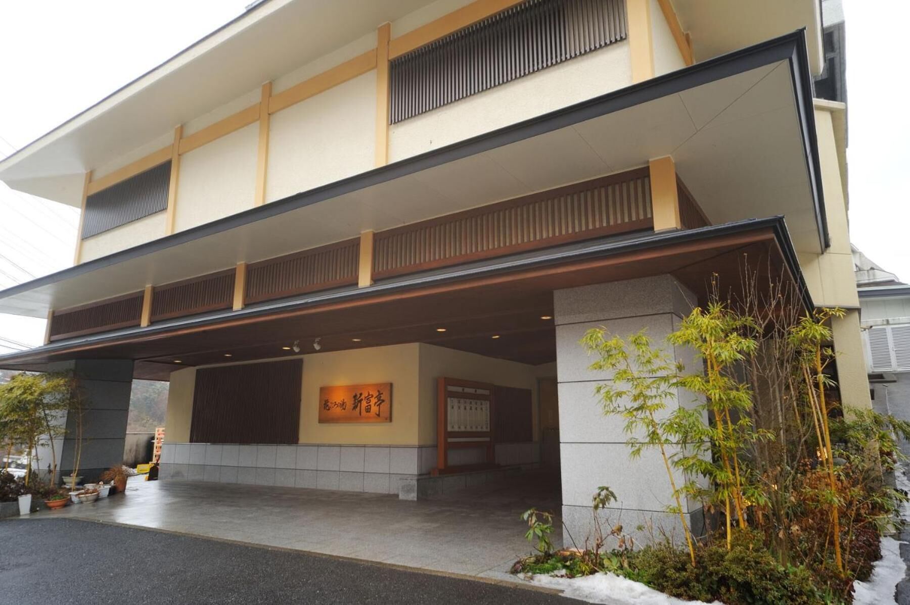 Un edificio moderno con entrada cubierta, un letrero con caracteres japoneses y un área ajardinada con bambú.