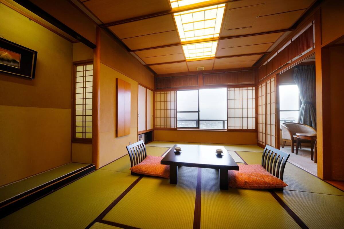 A tatami mat room with a low table and cushions, large windows, and traditional sliding doors.