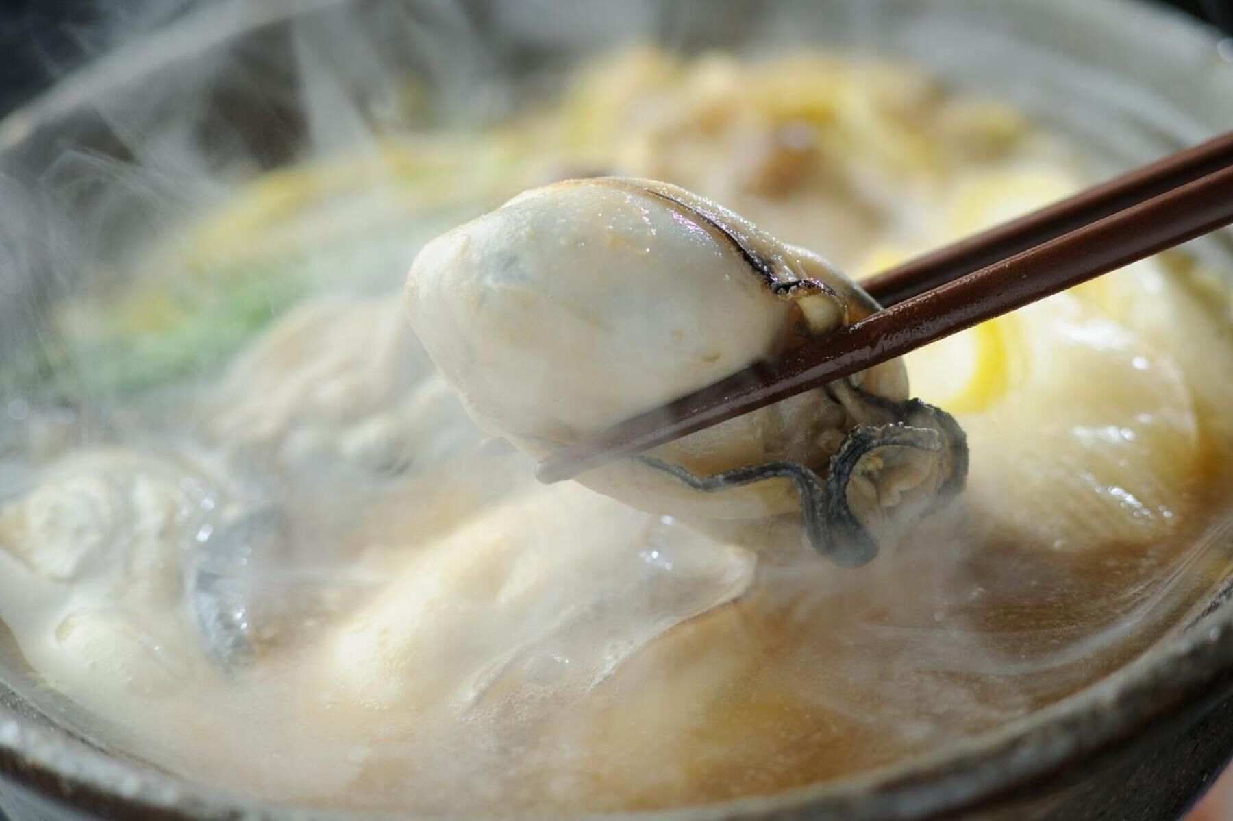 Primer plano de una olla humeante con fideos y dumplings que se sirven con palillos.