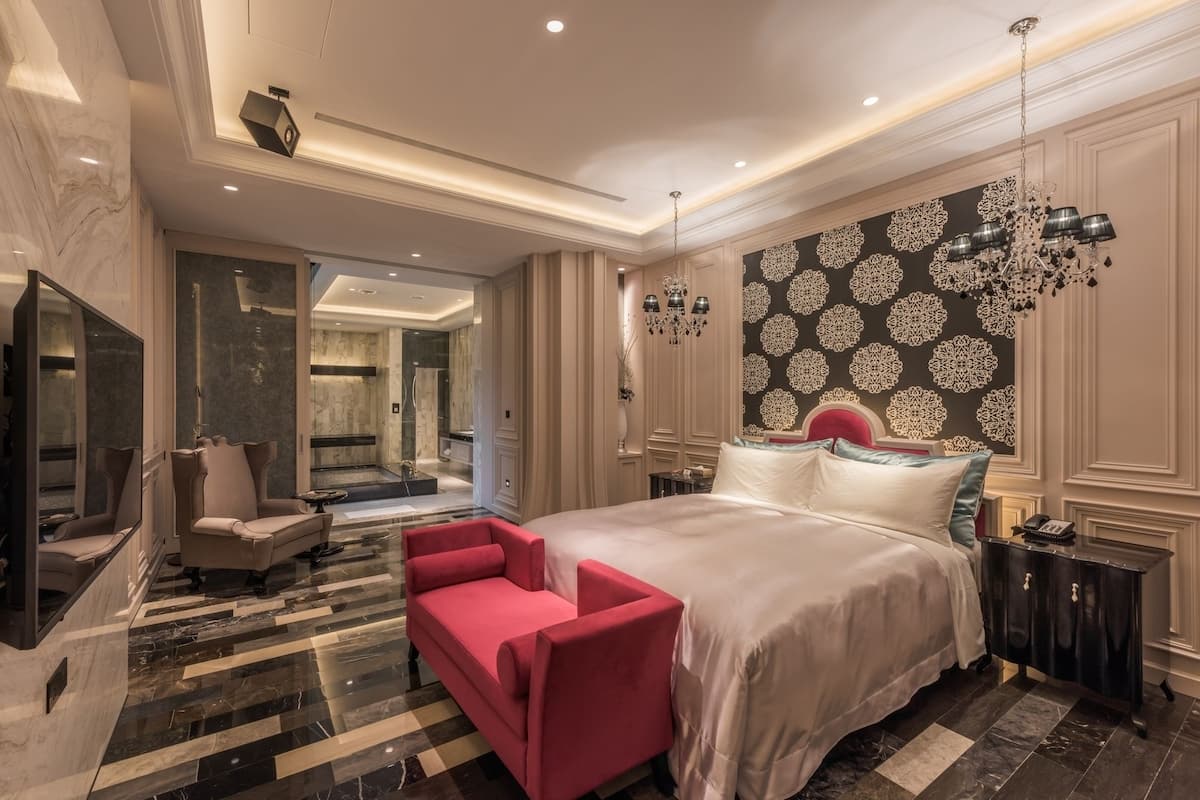 Ein luxuriöses Hotelzimmer mit einem großen Bett, einer roten Couch, einem Marmorboden und einer Wand mit aufwendigen Verzierungen.