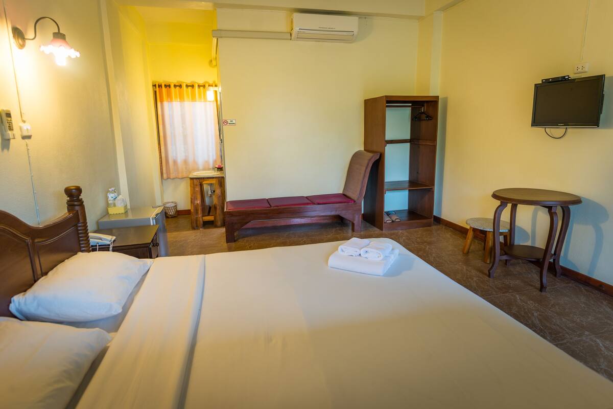 A hotel room with two beds, a desk, a chair, a small table, a TV, and a wardrobe.