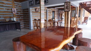 Un comedor rústico de madera con una mesa grande rodeada de sillas, taburetes de madera y una escalera al fondo.