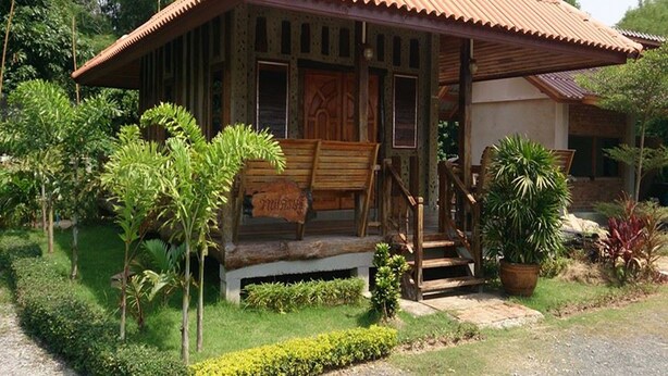 Una casa de madera tradicional con techo de tejas, un porche con banca y un jardín con diversas plantas.