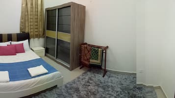 Un dormitorio con cama, mesita de noche, armario y un pequeño rincón de descanso.