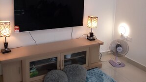 A living room with a flat-screen TV, two table lamps, a floor lamp, a fan, and a blue furry rug. - Khalish Homestay (Chemor)