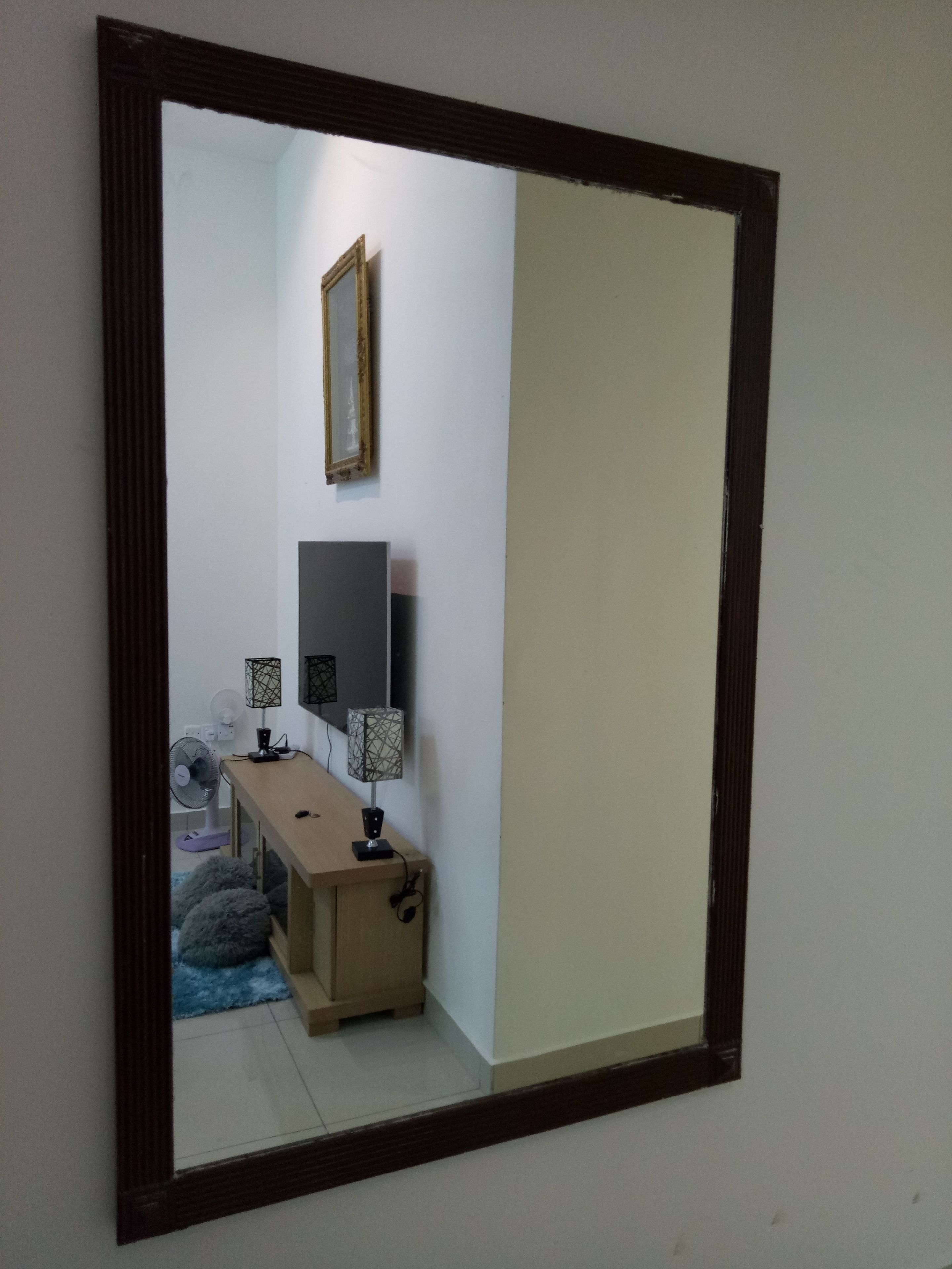 Una habitación con un espejo grande, un escritorio de madera, dos lámparas, un ventilador y una alfombra pequeña.