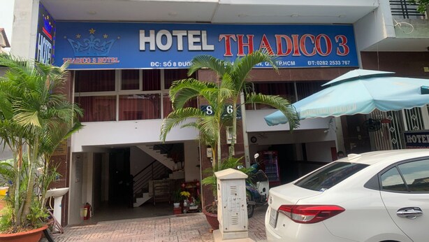 Ein Hotel namens THADICO3 mit einem blauen Schild, einer Treppe, die zum Eingang führt, und einem weißen Auto vor der Tür.